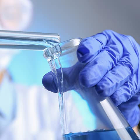 gloved hand pouring liquid into a beaker in a lab setting
